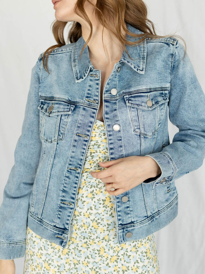 Person wearing a light blue denim jacket over a floral dress on a plain background