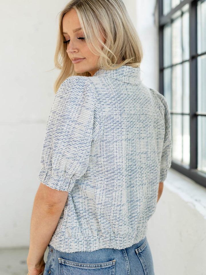 Woman wearing a textured blue and white shirt in a bright room.