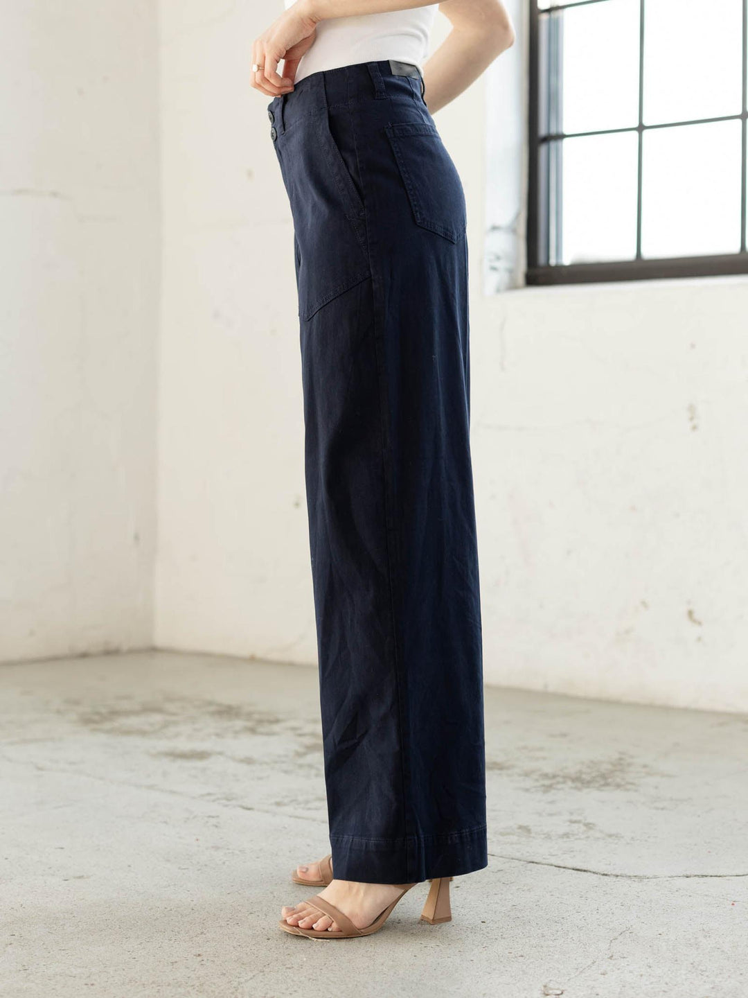 Person wearing navy wide-leg pants in a minimalistic room with white walls and a large window.