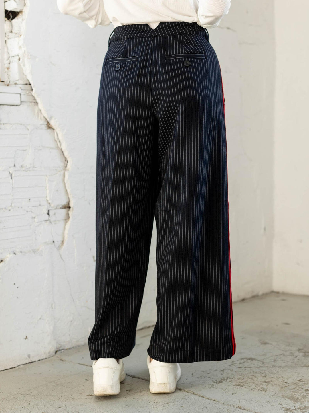 Person wearing black pinstripe pants with a red stripe against a white brick wall.