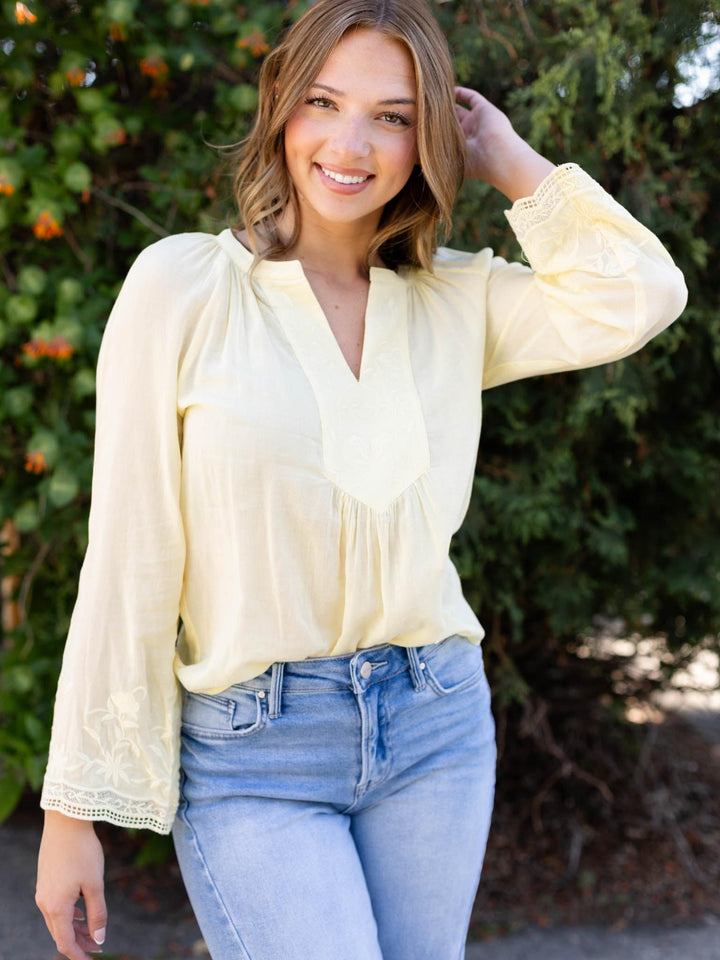 Woman in a yellow Lovestitch raglan bell sleeve blouse with floral embroidery and light wash jeans.