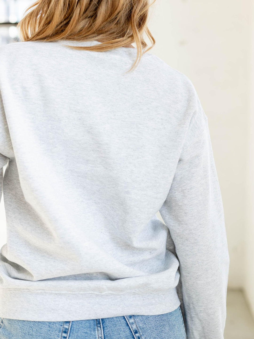Person wearing a light gray sweatshirt and blue jeans against a neutral background