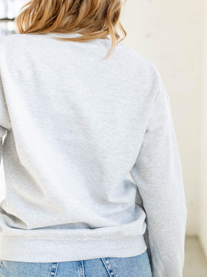 Person wearing a light gray sweatshirt and blue jeans against a neutral background
