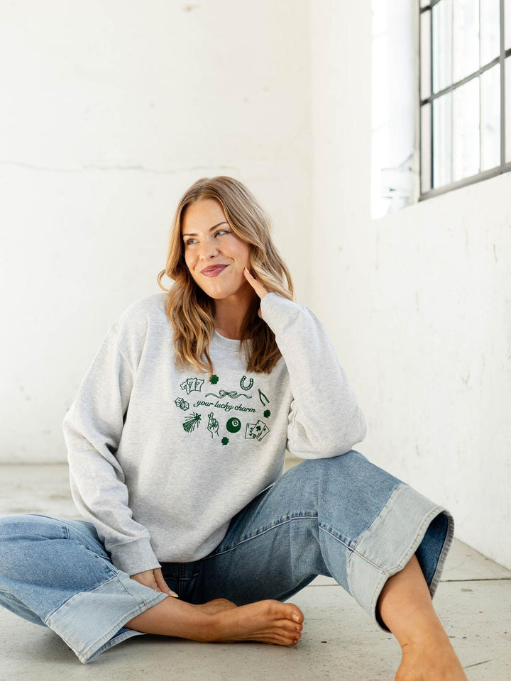 Woman wearing a white sweatshirt with green text and graphics, sitting on the floor in a bright room.