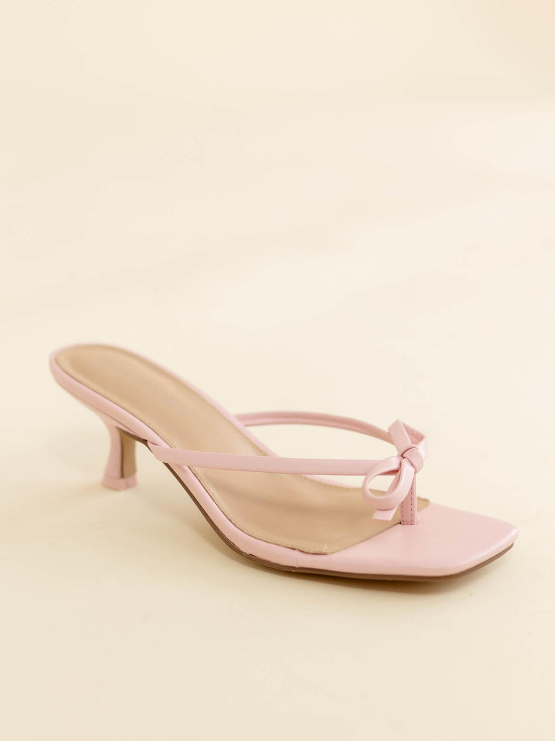 Pink high-heeled sandal with a bow on a light pink background