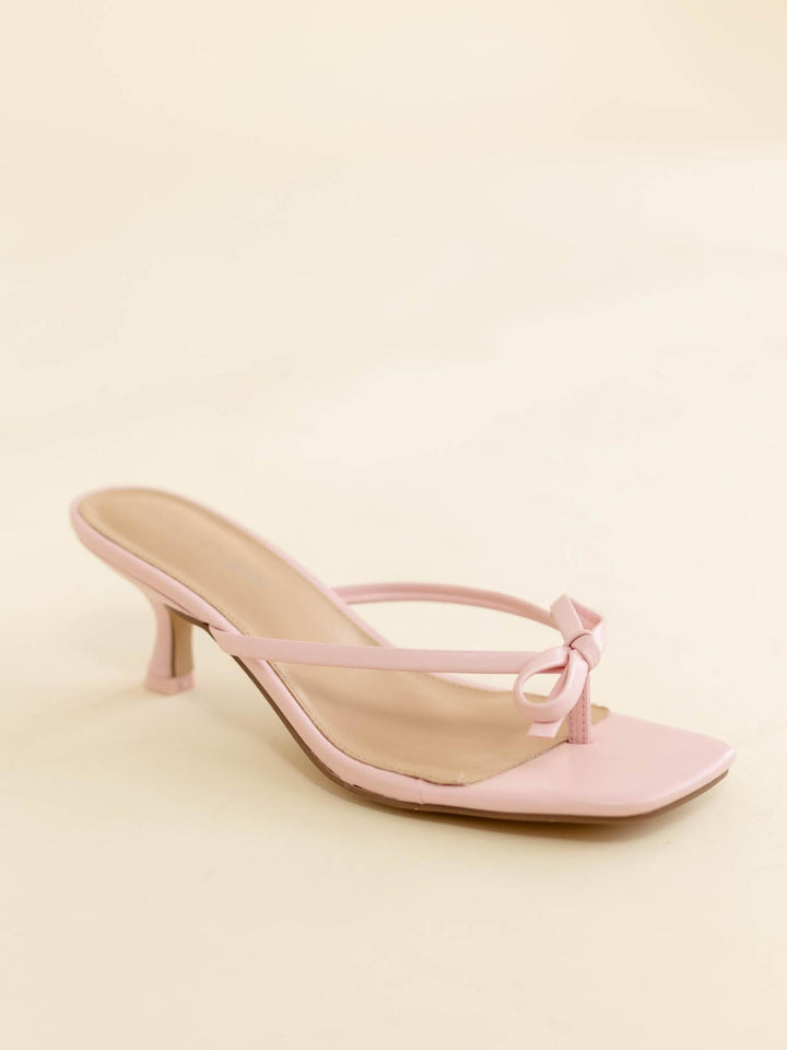 Pink high-heeled sandal with a bow on a light pink background