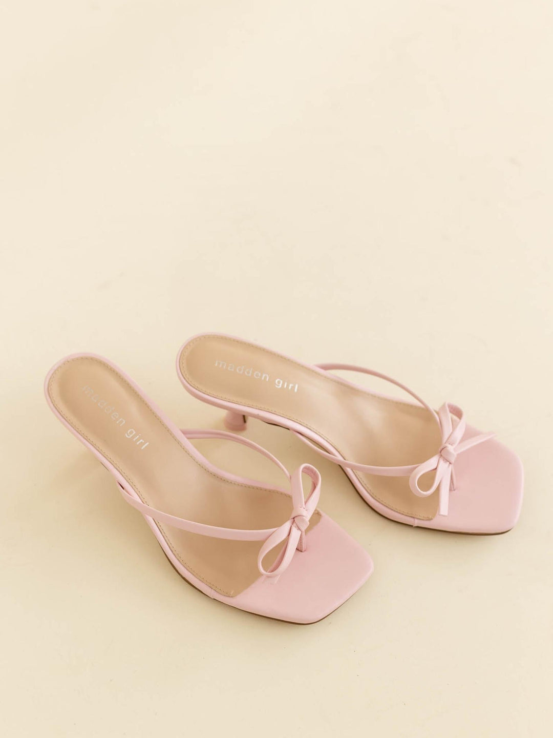 Pair of pink high-heeled shoes with bow detail on a beige background