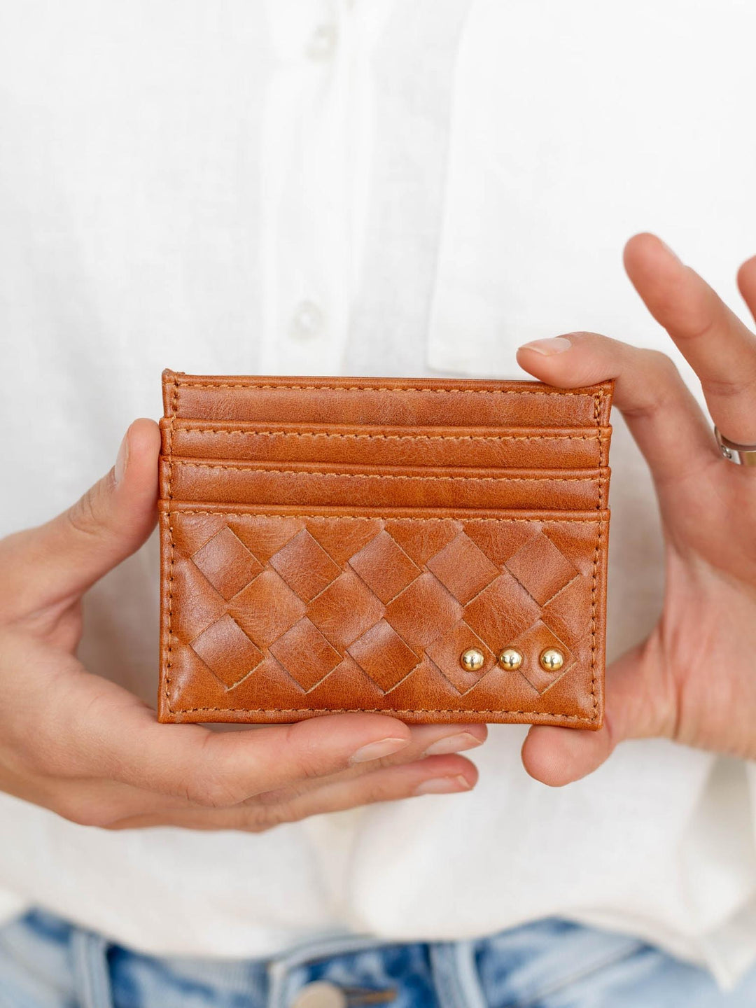 Brown woven cardholder held by hands against a white background