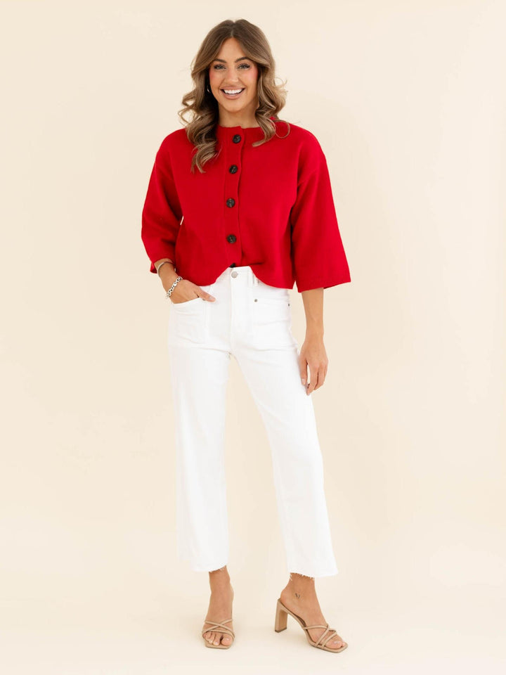 Woman wearing a red jacket and white pants on a beige background