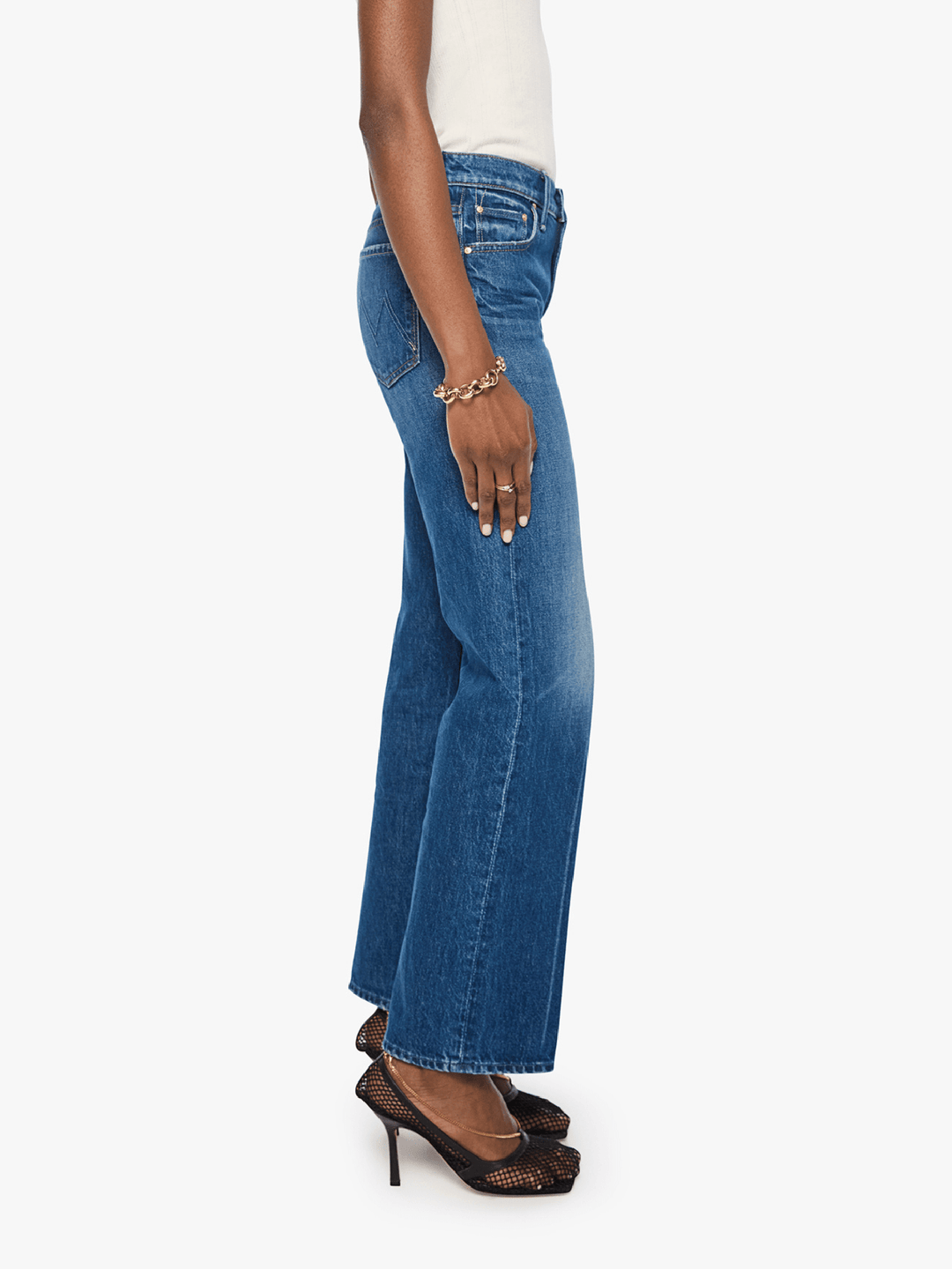 A side profile view of a model wearing blue wide-leg denim jeans, a white top, and black high-heeled sandals against a plain white background.