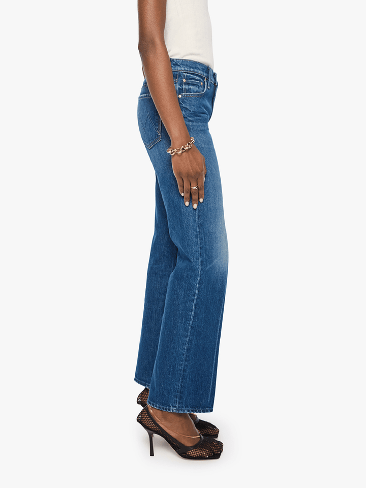 A side profile view of a model wearing blue wide-leg denim jeans, a white top, and black high-heeled sandals against a plain white background.