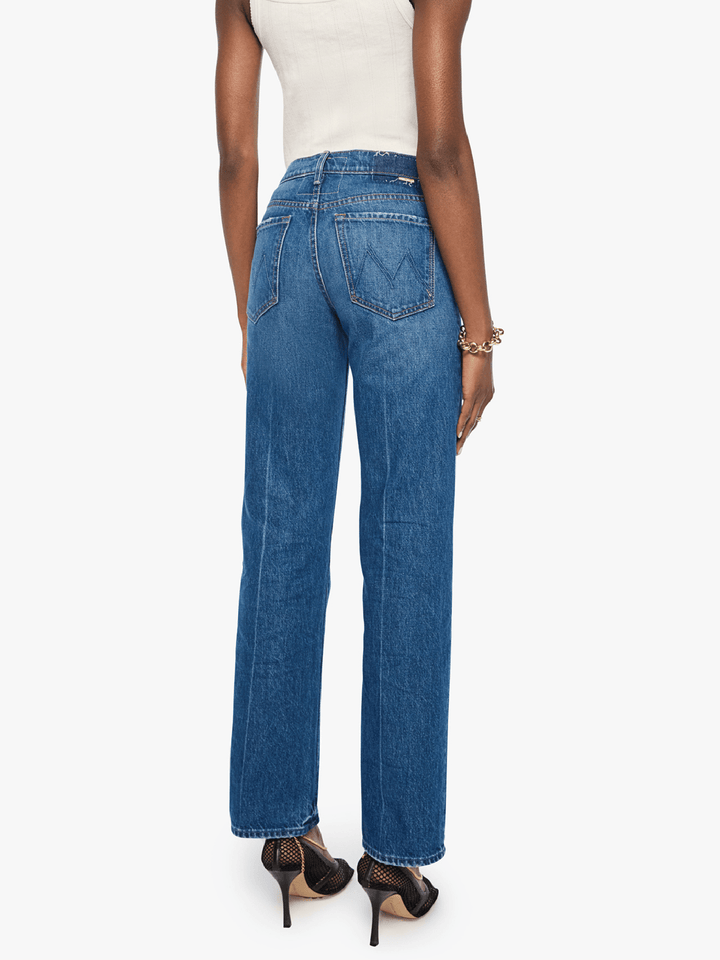 A model shown from the back wearing high-waisted, wide-leg blue denim jeans, a white ribbed tank top, and black high-heeled sandals against a plain white background.