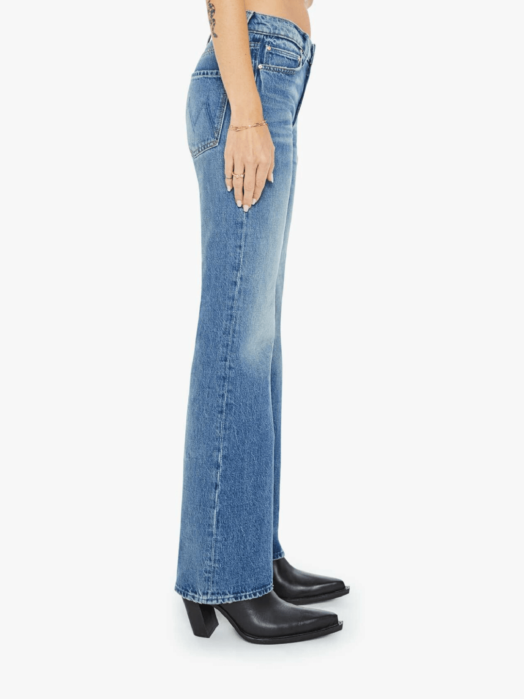 Side view of a model wearing light blue high-waisted flare jeans with black pointed-toe heeled boots, shown against a plain light gray studio background.