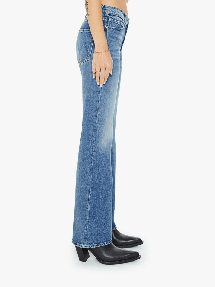 Side view of a model wearing light blue high-waisted flare jeans with black pointed-toe heeled boots, shown against a plain light gray studio background.