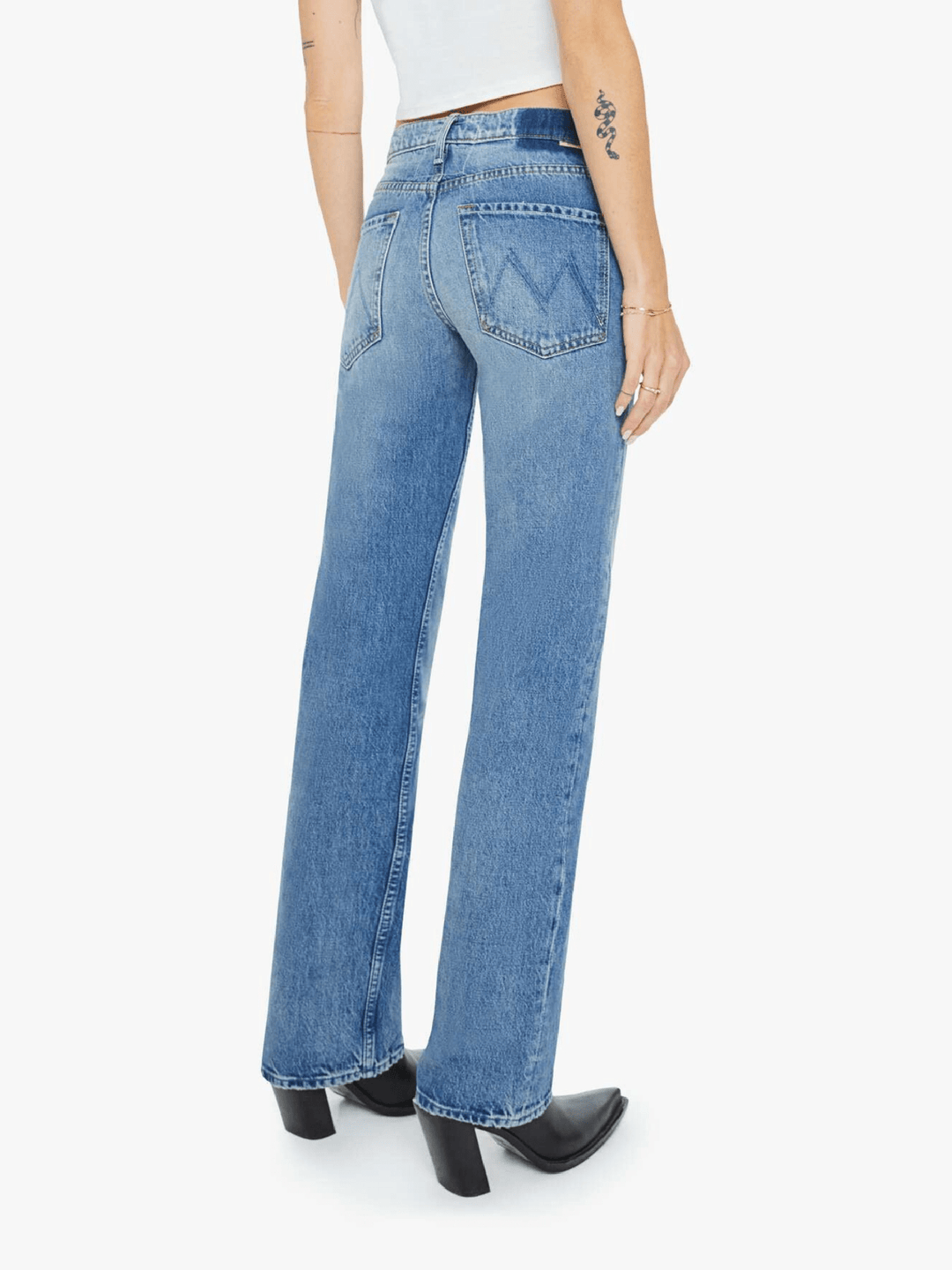 A person shown from the back wearing light blue wide-leg denim jeans, a white cropped top, and black heeled boots against a plain light gray studio background.