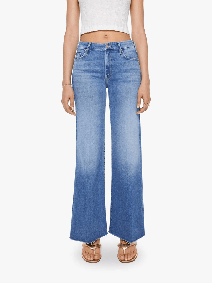 A model wearing high-waisted, wide-leg blue jeans with a faded wash and a gradient fade towards the hem, paired with a white crop top and metallic sandals, against a plain white background.