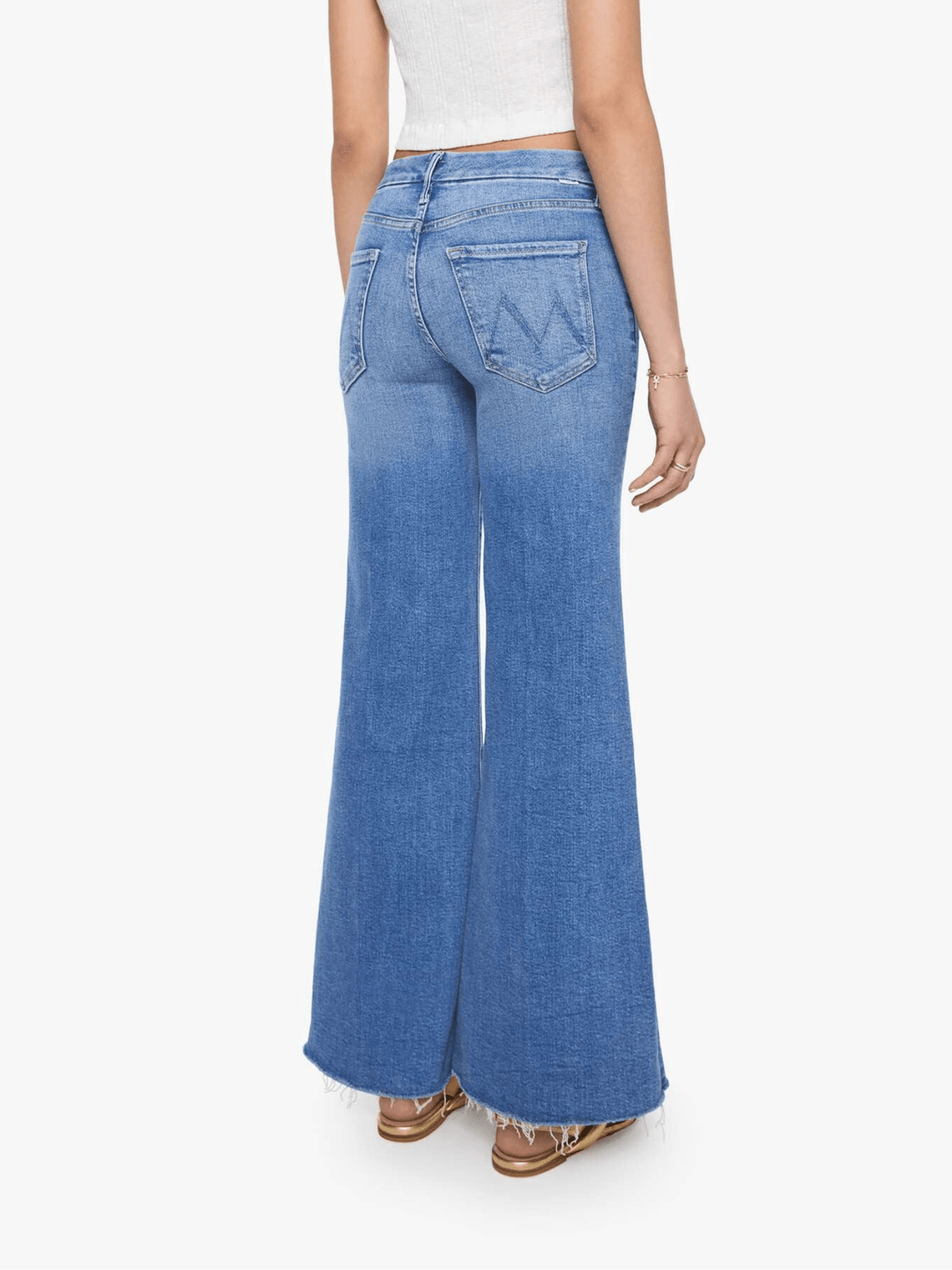 A person shown from the back wearing light blue wide-leg denim jeans with a frayed hem, paired with a white cropped top and brown sandals, against a plain light gray studio background.