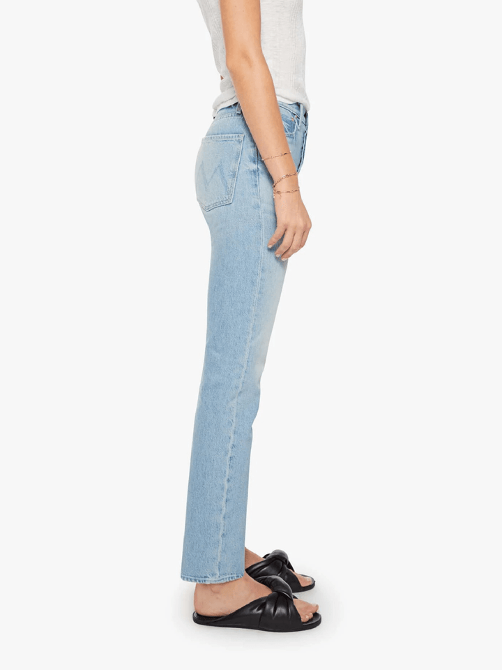A side profile view of a model wearing light-wash blue denim jeans, a white top, and black slide sandals against a plain white background.