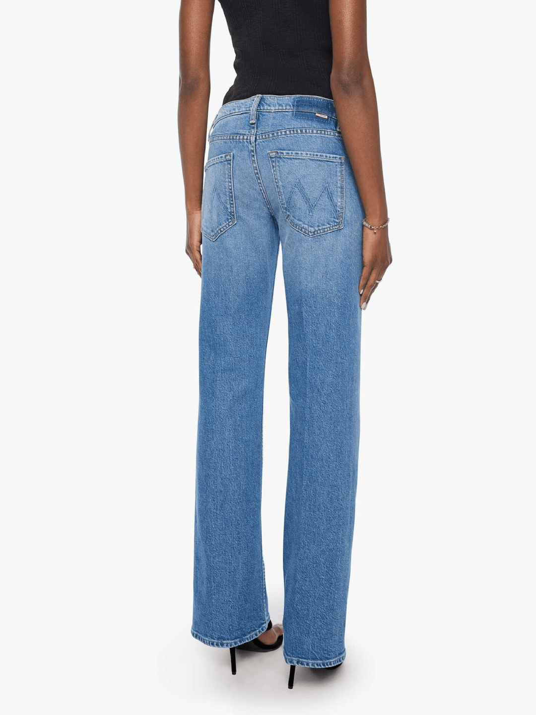 Rear view of a model wearing light blue wide-leg denim jeans with a black top and black heels, shown against a plain white studio background.
