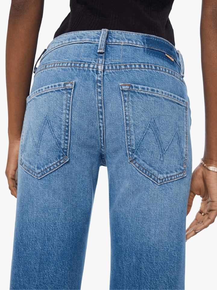 Close-up back view of a person wearing light blue denim jeans with a black top, showing the back pockets and waistband details against a plain light background.
