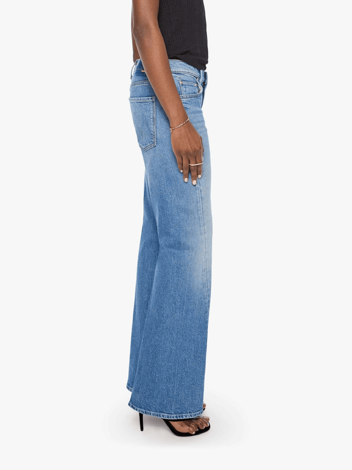 A side profile view of a model wearing light-wash blue wide-leg denim jeans, styled with a black top and black heeled sandals against a plain white background.