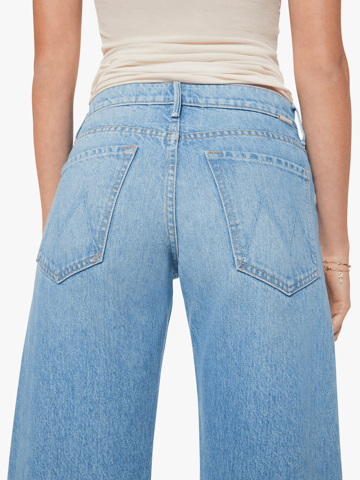 Rear view of a person wearing light-wash blue wide-leg jeans with a cream ribbed top, shown against a plain light background.