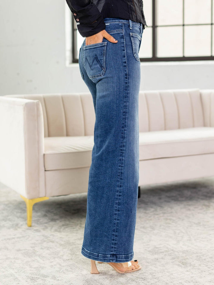 Person wearing blue jeans standing in a room with a beige sofa and large window.