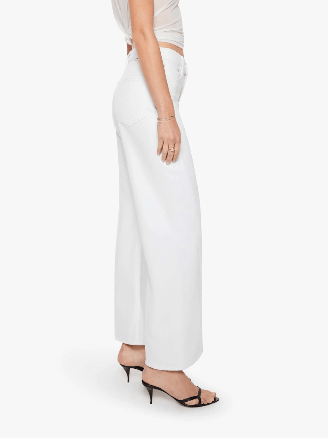 A model shown from the waist down wearing white wide-leg cropped pants, a light beige crop top, and black strappy high-heeled sandals against a plain white background.