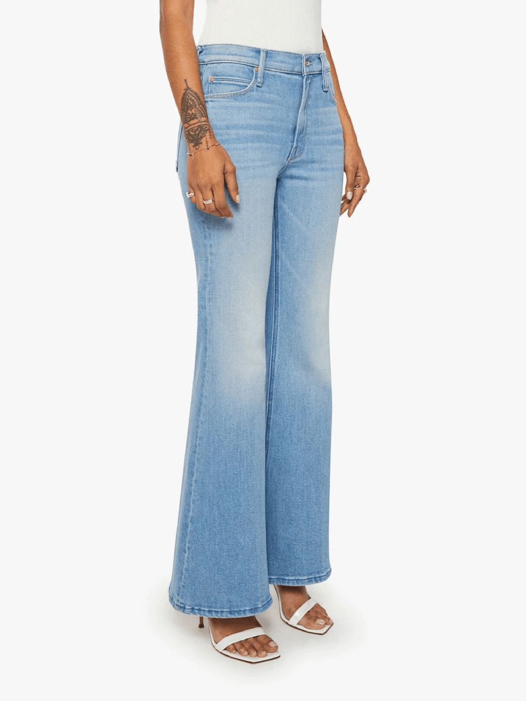 A model wearing light blue high-waisted flare jeans with a faded wash, styled with a white top and white heeled sandals against a plain white background.