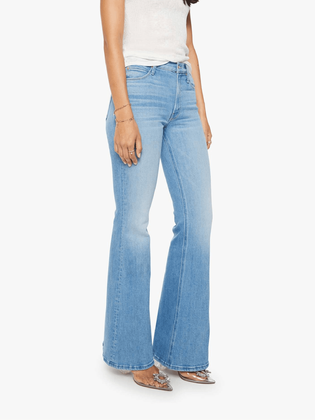 A model wearing light blue high-waisted flare jeans with a faded wash, styled with a white top and metallic flat shoes against a plain white background.