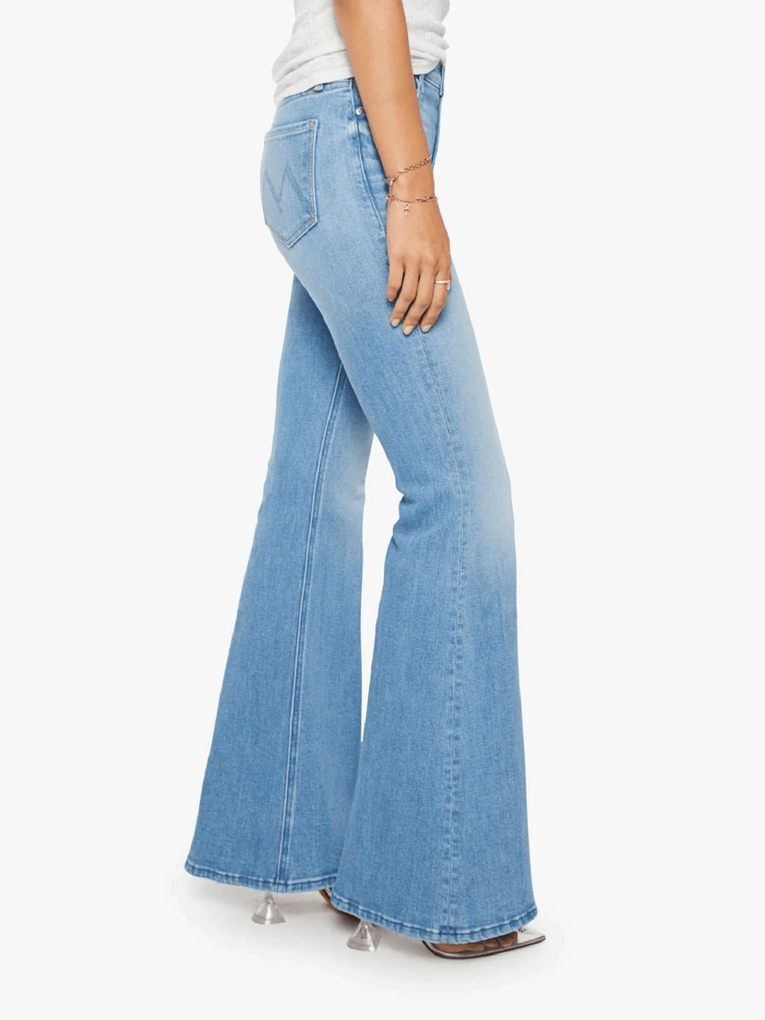 Light blue wide-leg flare jeans shown on a model from the side, paired with a white top and clear high-heeled sandals against a plain white background.