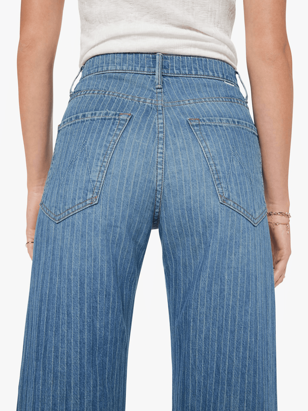 Rear view of a person wearing light blue denim jeans with a subtle vertical stripe pattern, paired with a white top against a plain light background.