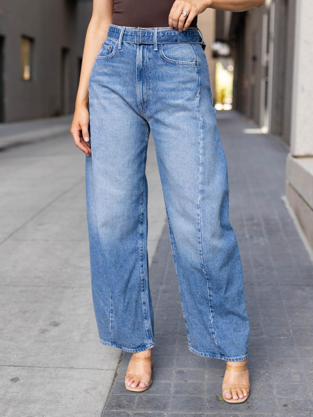 A person wearing light blue wide-leg denim jeans with a faded wash, standing on a city sidewalk.