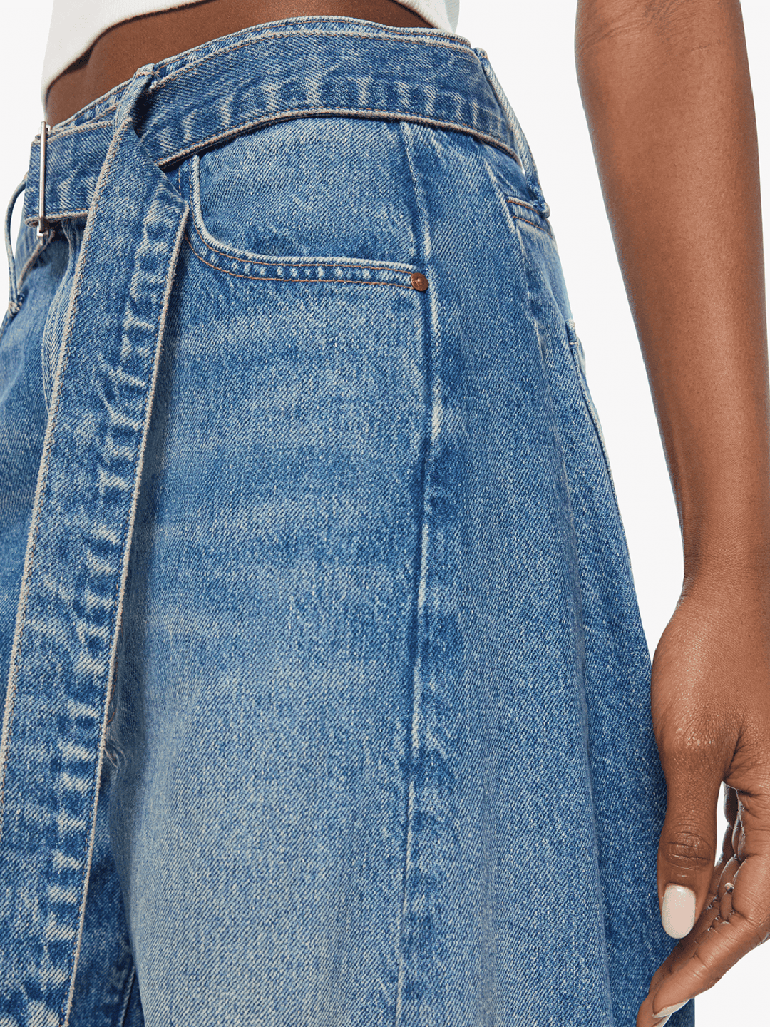 Close-up of a person wearing a pair of high-waisted, wide-leg blue denim jeans with a front button closure and belt loops, shown against a plain white background.
