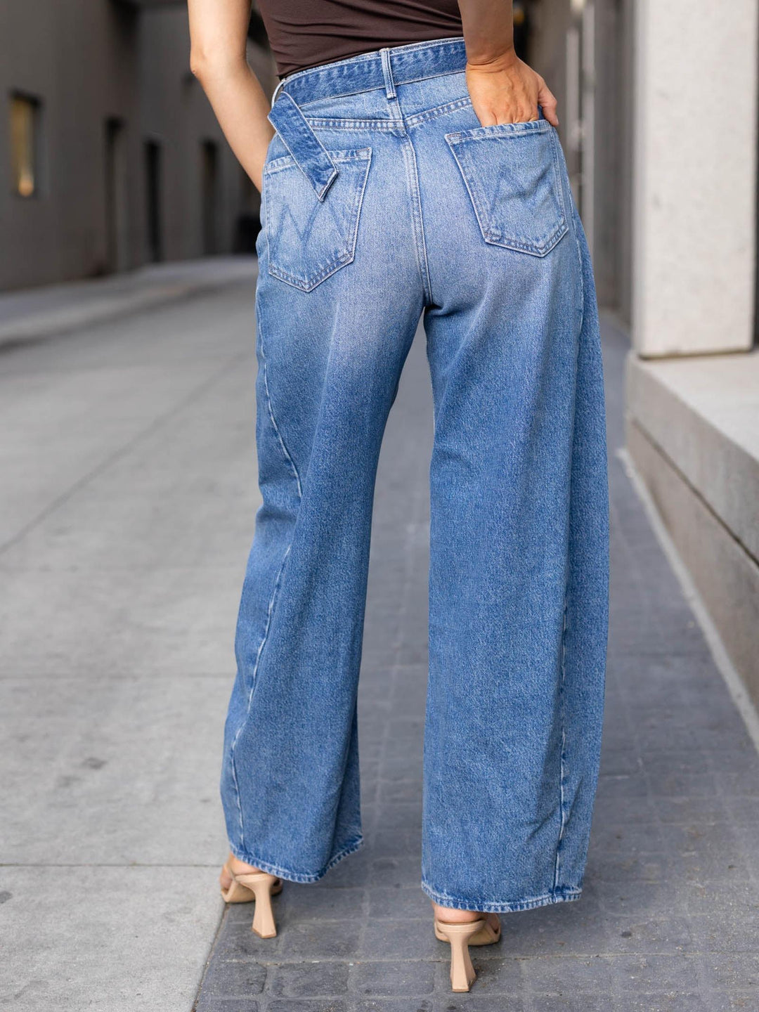 A person shown from the back wearing light blue wide-leg denim jeans, standing on a paved outdoor walkway.