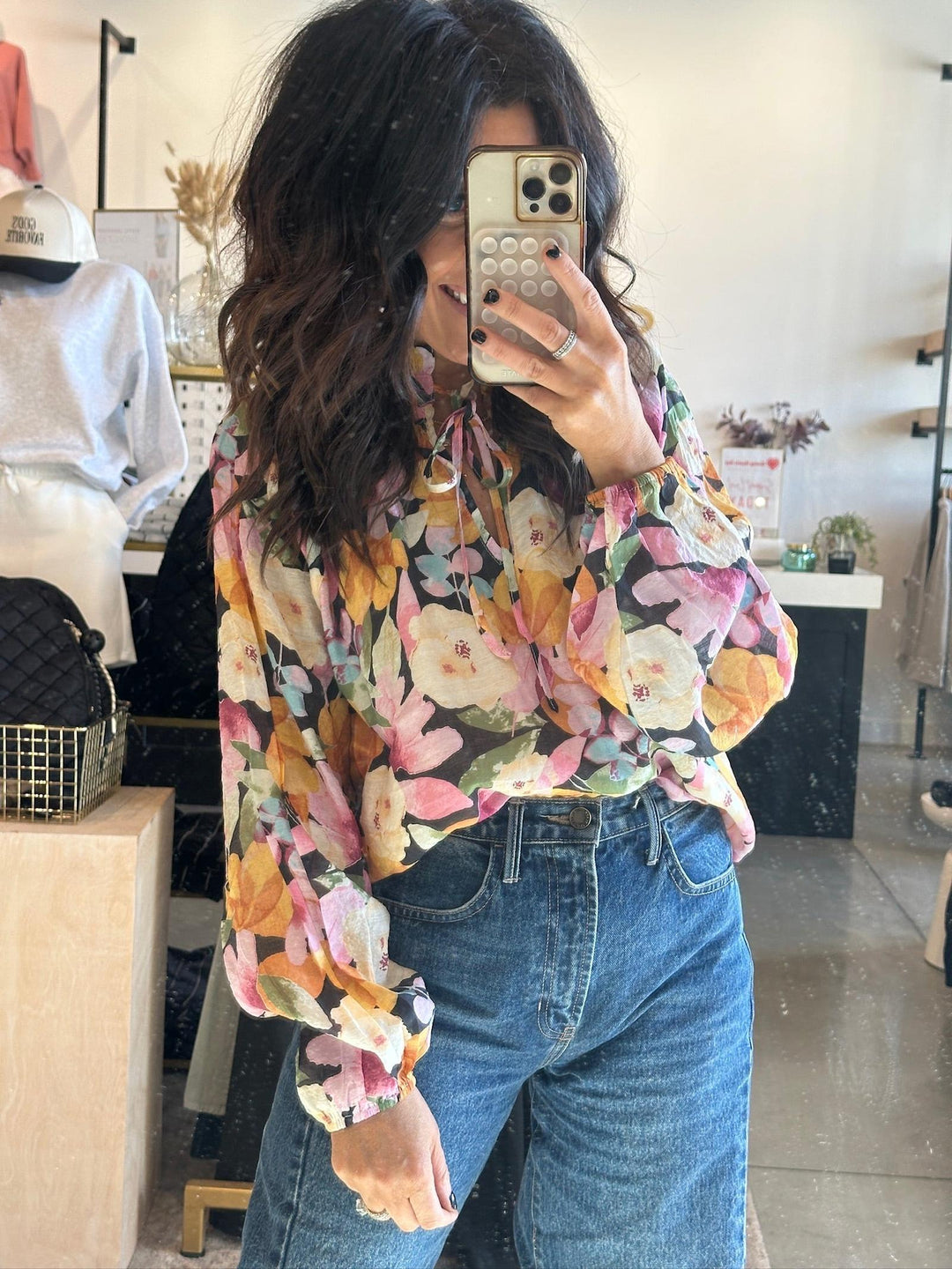 Person wearing a colorful floral blouse and blue jeans taking a mirror selfie.