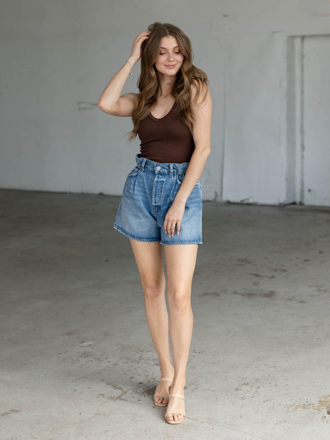 Woman wearing AGOLDE Outbreak Lyonne Paper Bag Shorts in medium wash denim with a brown tank top.