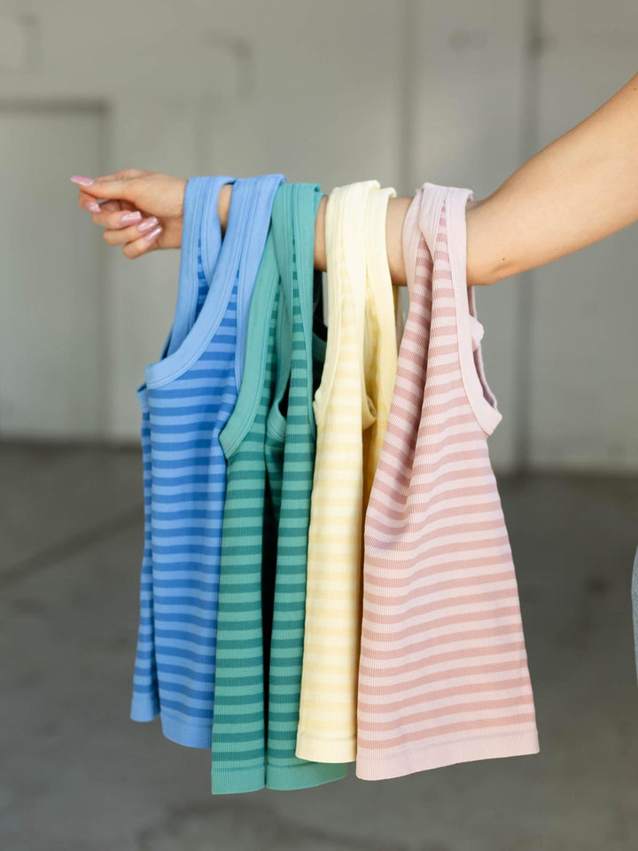 Hand holding four striped tank tops in blue, green, yellow, and pink.