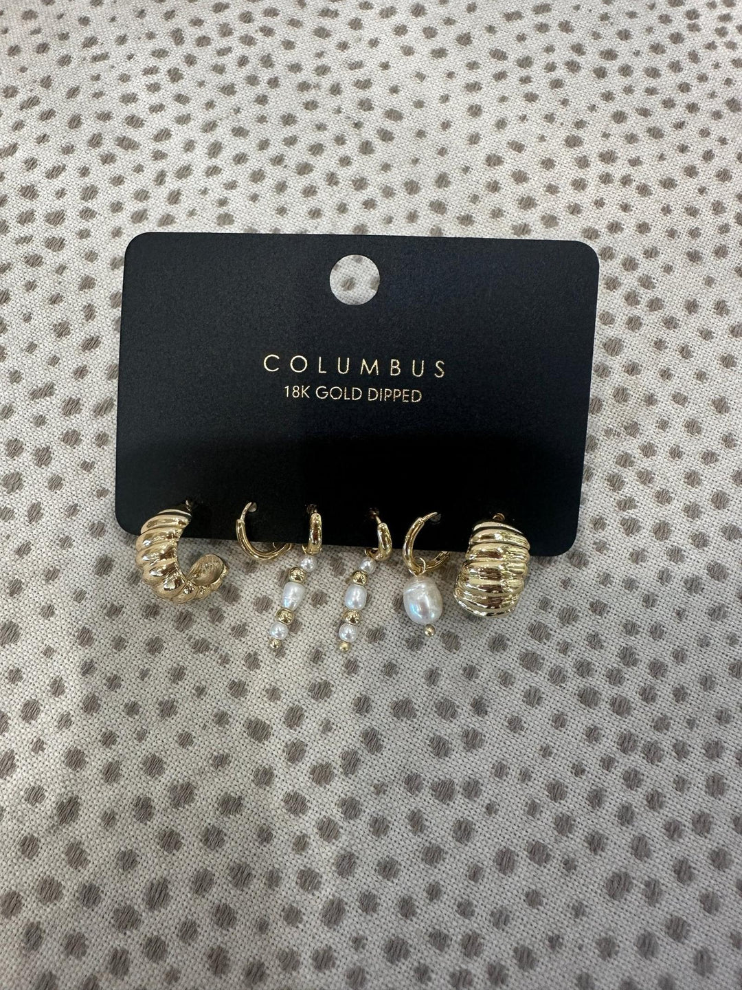 Gold and pearl earrings on a Columbus branded card against a patterned background