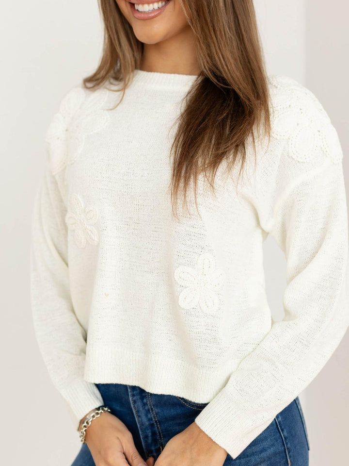 Woman wearing a white sweater and blue jeans against a plain background