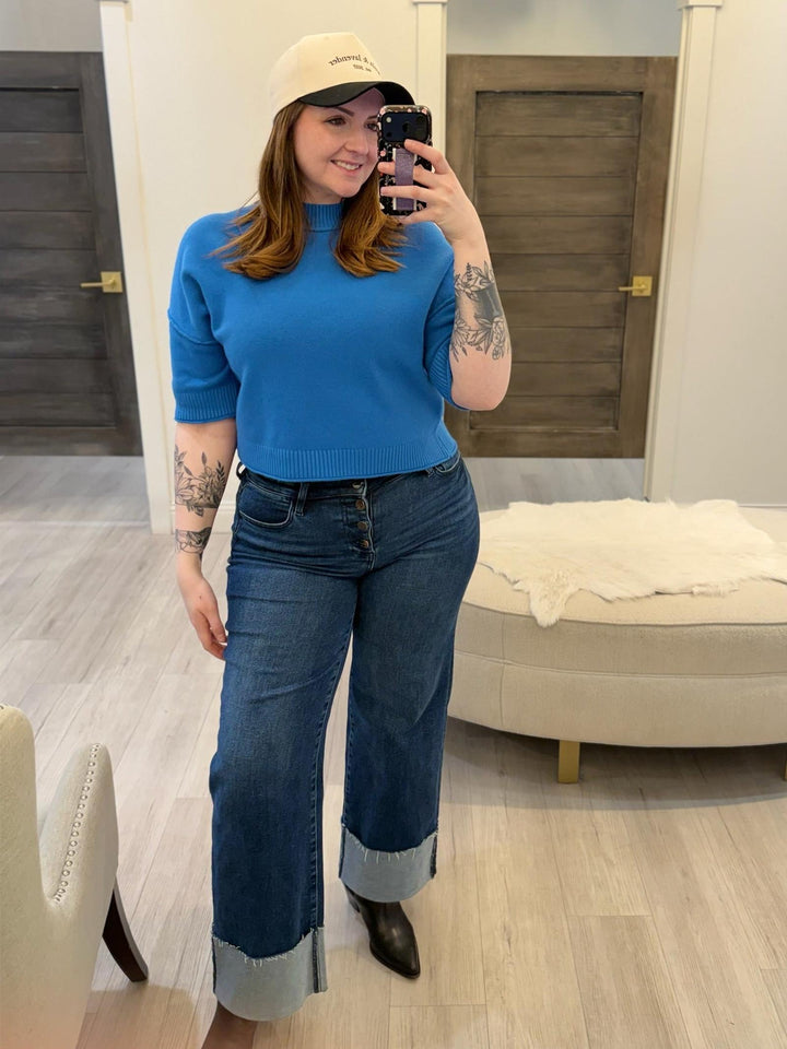 Woman in blue PINCH Short Sleeve Sweater Top, dark wash jeans, and a baseball cap.