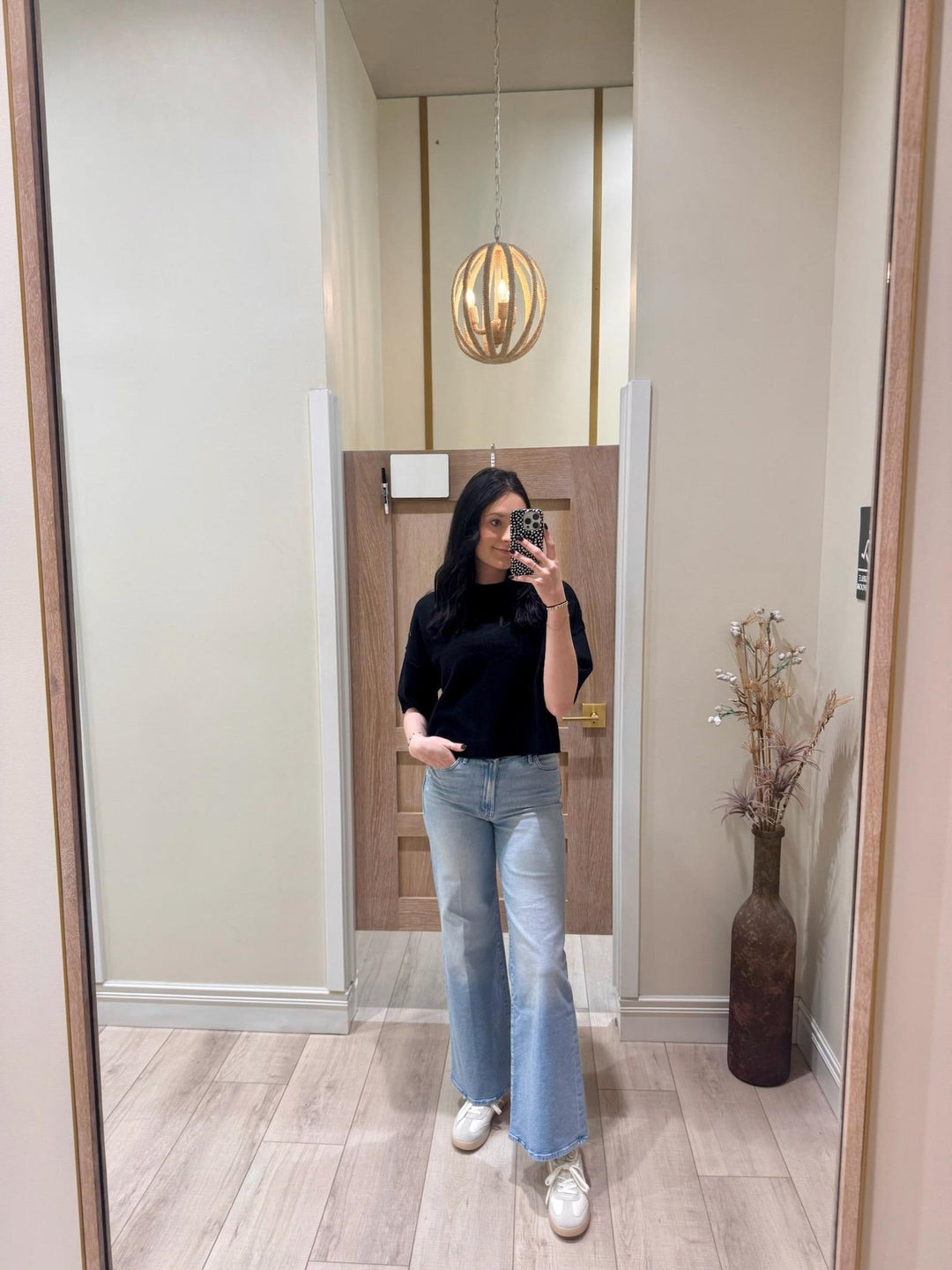 Woman in black PINCH Short Sleeve Sweater Top, light wash jeans, and white sneakers.