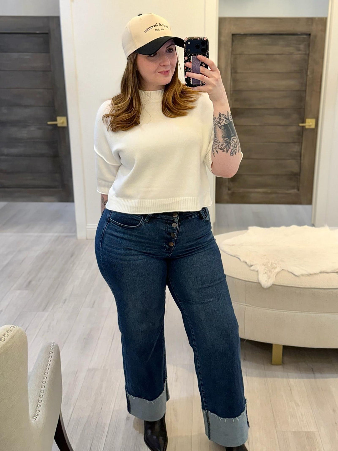 Woman wearing a cream PINCH Short Sleeve Sweater Top, dark wash jeans with rolled hems, and a baseball cap.