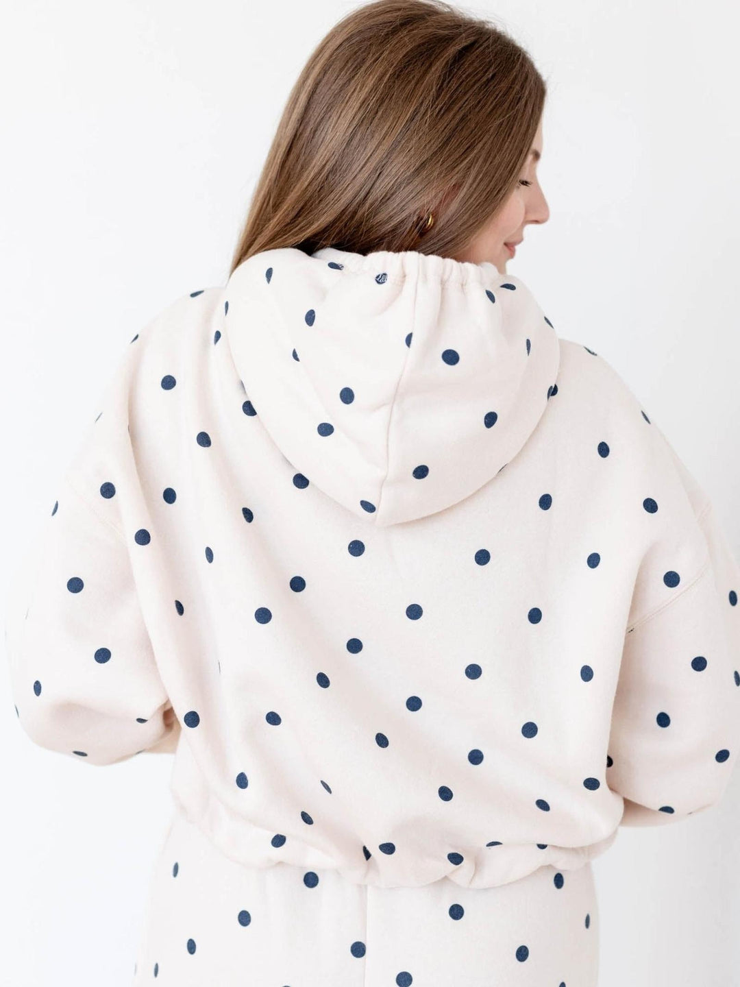 Woman in a beige polka dot cropped hoodie with gathered waist and drop shoulders, viewed from the back.