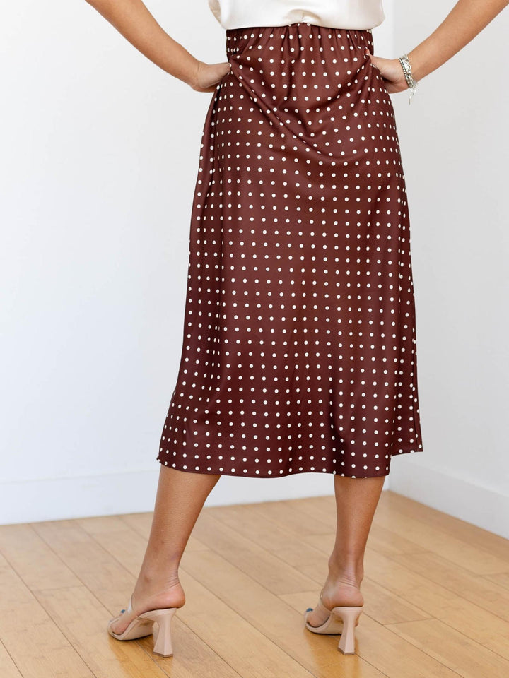 Person wearing a brown polka dot skirt on a plain background
