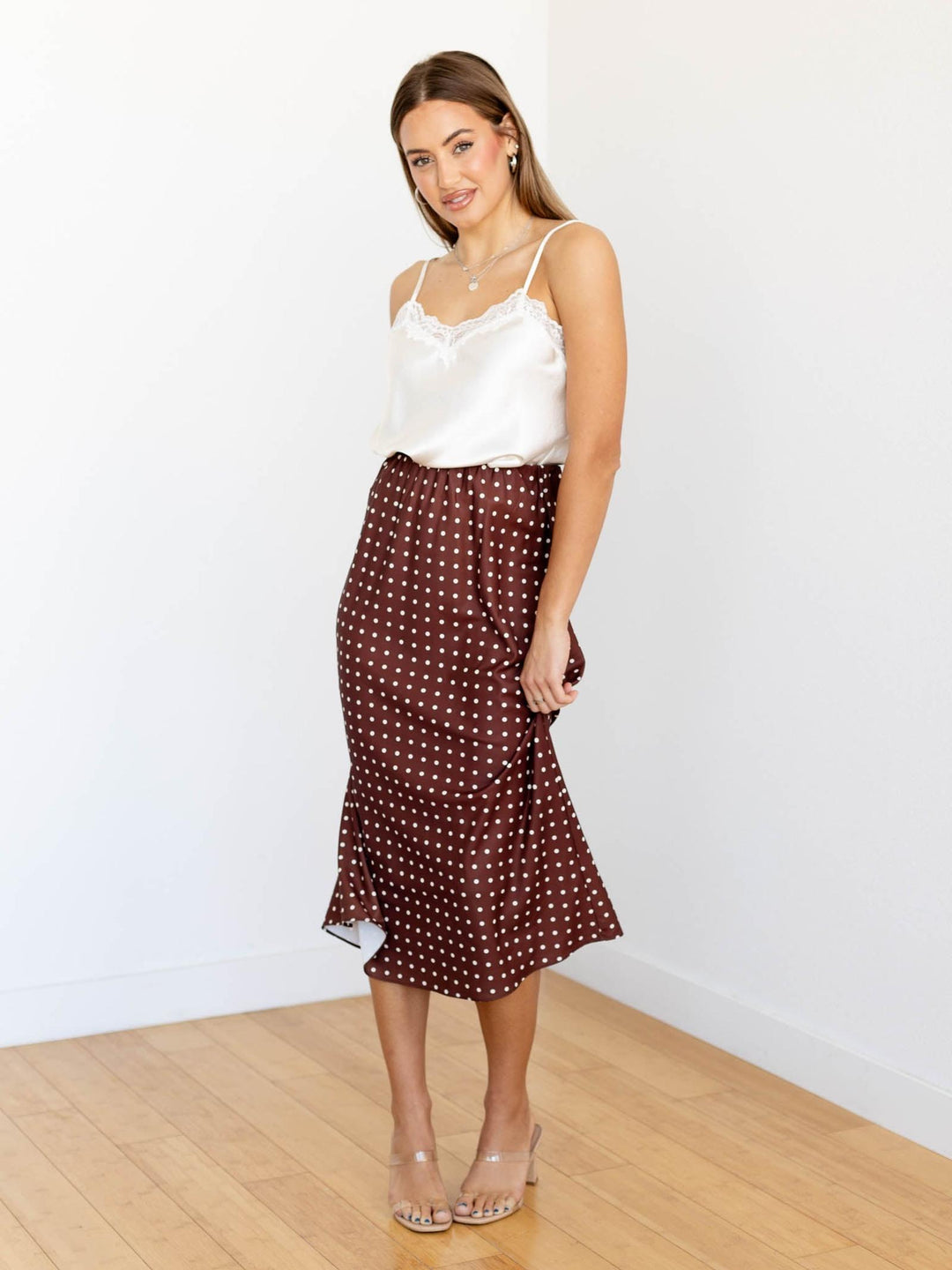 Woman wearing a white top and brown polka dot skirt on a plain background
