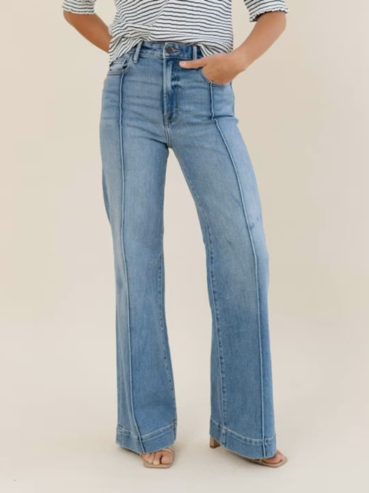 Person wearing blue flared jeans and a striped shirt on a beige background