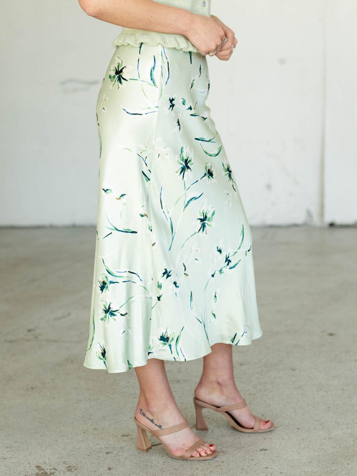Person wearing a light green floral skirt with a neutral background