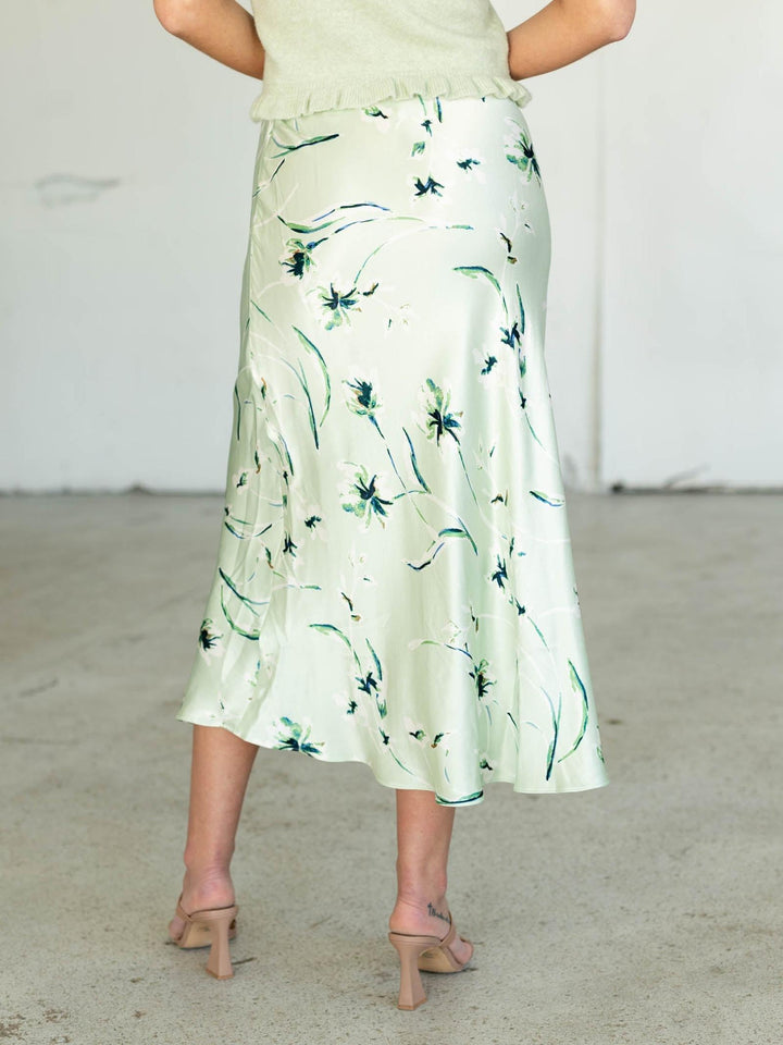 Person wearing a light green floral skirt on a plain background