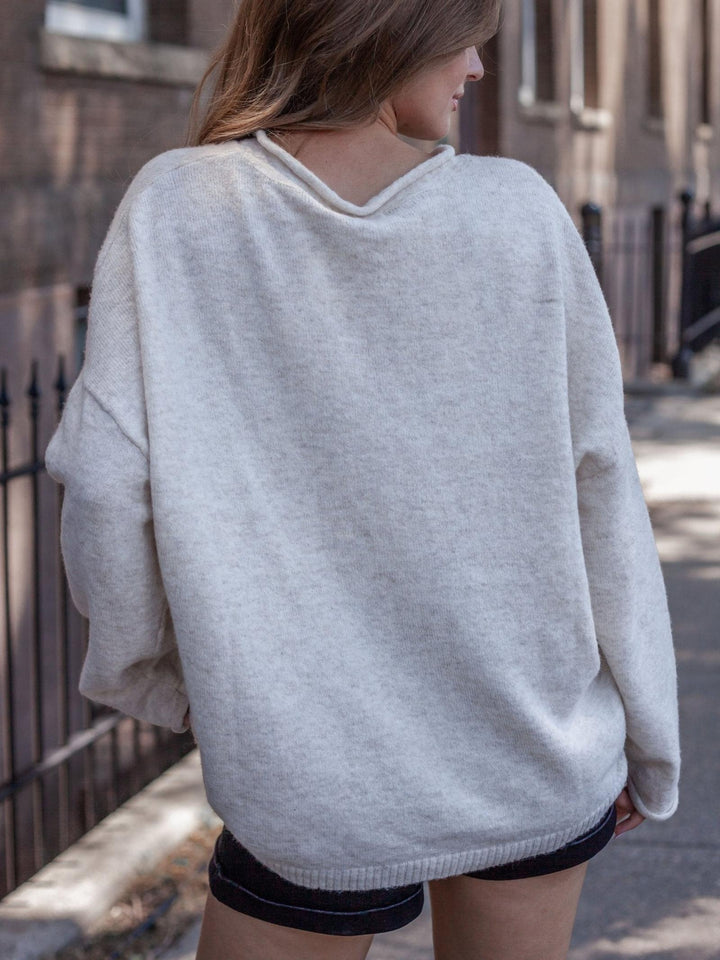 A woman wearing an oversized light gray knit sweater, shown from the back in an outdoor urban setting.